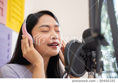an asian female singer wearing and holding headphones while singing an asian female singer wearing and holding headphones while singing 80488195