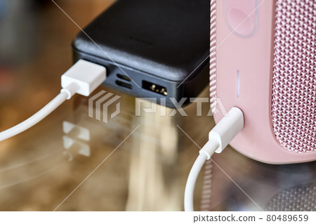 Power bank charges portable audio speaker using a USB cable on a glass surface. Close-up, selective focus Power bank charges portable audio speaker using a USB cable on a glass surface. Close-up, selective focus 80489659