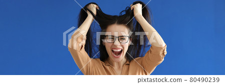 Angry woman with glasses tearing her hair on blue background 80490239