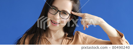 Young woman in glasses holding index finger near forehead on blue background 80490240
