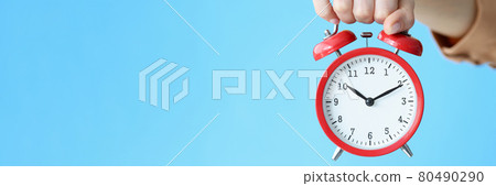Woman holding red alarm clock in her hand on blue background closeup 80490290