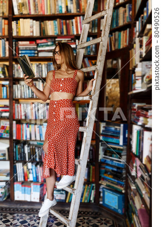 Happy student girl or woman with picking up books in library. Young woman casual daily lifestyle standing with books on wooden stairs joyful. 80490526