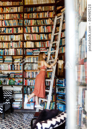 Happy student girl or woman with picking up books in library. Young woman casual daily lifestyle standing with books on wooden stairs joyful. 80490528