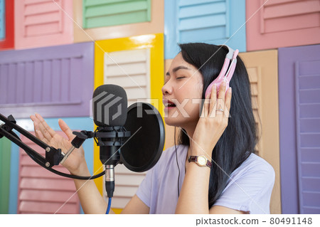 singer wearing headphones singing using microphone against colored wooden wall background singer wearing headphones singing using microphone against colored wooden wall background 80491148