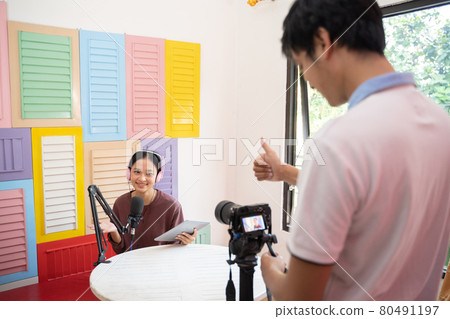 a male cameraman with a thumbs up sign ready to start recording using a camera to a girl wearing headphones a male cameraman with a thumbs up sign ready to start recording using a camera to a girl wearing headphones 80491197