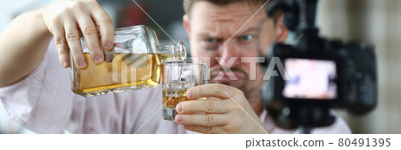 Man with hematoma under his eye pouring alcohol and taking video camera 80491395