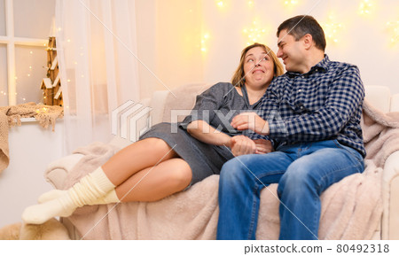portrait of adult romantic couple sitting on a couch at home, holiday lights on a wall portrait of adult romantic couple sitting on a couch at home, holiday lights on a wall 80492318