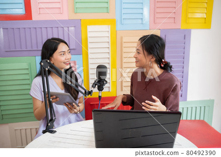 two women chatting during podcast using microphone and a tablet 80492390