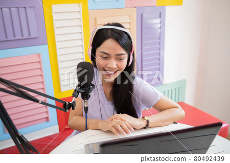 cheerful girl using laptop and wearing headphones while talking into microphone during podcast cheerful girl using laptop and wearing headphones while talking into microphone during podcast 80492439