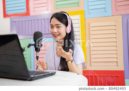 woman wearing headphones talking in front of microphone with hand gesture 80492493