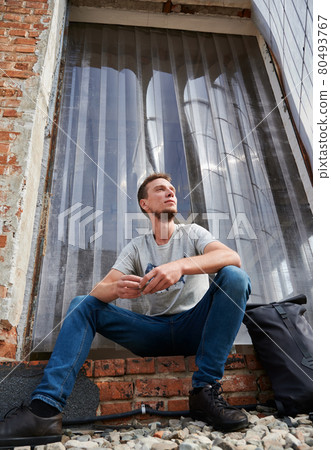 Smiling male is sitting on stairs outdoors. Smiling male is sitting on stairs outdoors. 80493767