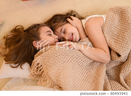 girls is lying on the floor and talking or sleeping, and cover themselves with a blanket, home interior decorated with holiday lights and gifts 80493941