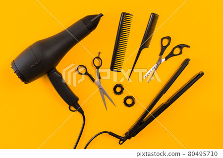Black hair dryer, comb and scissors on yellow paper background. Top view Black hair dryer, comb and scissors on yellow paper background. Top view 80495710