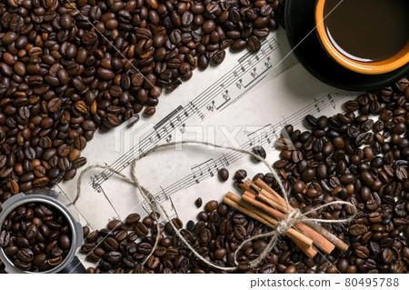 Coffee beans, cinnamon sticks and cup of brewed coffee on sheet music background, view from above with space for text 80495788
