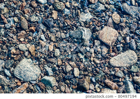 Transparent water in river with rocky bottom, fast flow. Nature outdoors close-up. Sun glare on smooth stones at bottom stream. 80497194