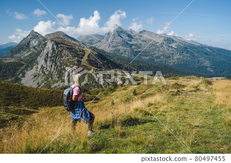 Woman with backpack enjoying view over Passo Rolle, - Italy , Dolomites. Scenery from summer vacation Woman with backpack enjoying view over Passo Rolle, - Italy , Dolomites. Scenery from summer vacation 80497455