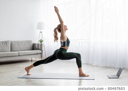 Portrait of young balanced woman in sportswear doing yoga pose on mat at home with notebook beside 80497683