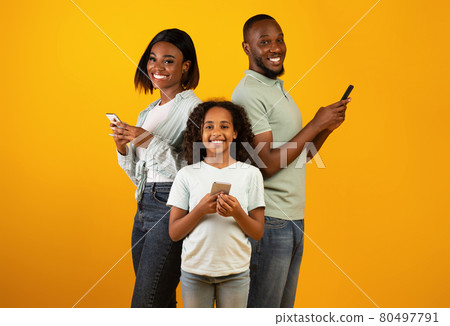 Modern family. Excited african american father, mother and daughter using smartphones over yellow background 80497791