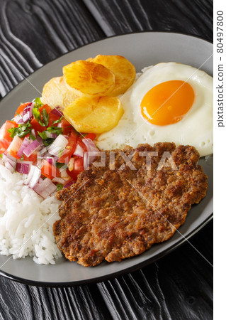 Silpancho is an incredible Bolivian meal made of rice and is topped with a pan fried burger, salsa, fried potatoes, and egg closeup in the plate. Vertical 80497800