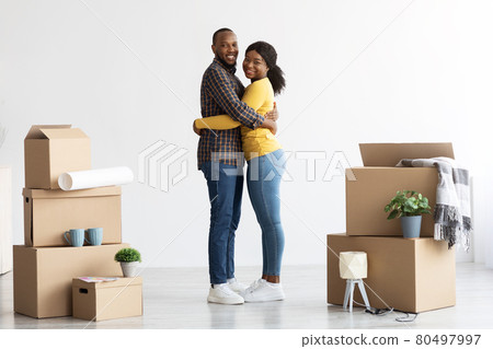 Happy Black Spouses Embracing At New Home Among Cardboard Boxes With Belongings 80497997