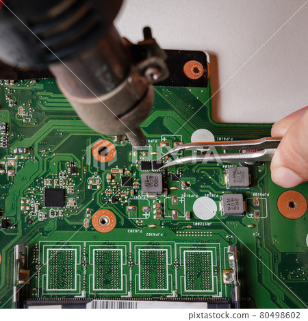 Repairman is using tweezers and hot air blower to fix motherboard. 80498602
