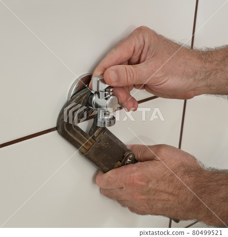 Plumber fixing  tap in a bathroom or kitchen using adjustable wrench 80499521