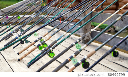 Many fishing rods on the wooden pier by the river or lake on a sunny day Many fishing rods on the wooden pier by the river or lake on a sunny day 80499799