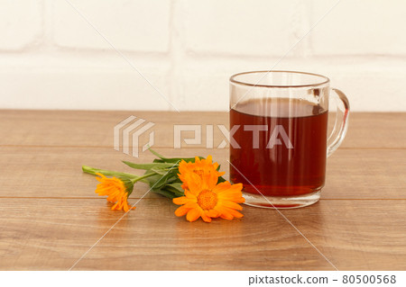 Glass cup of tea with yellow marigold flowers 80500568