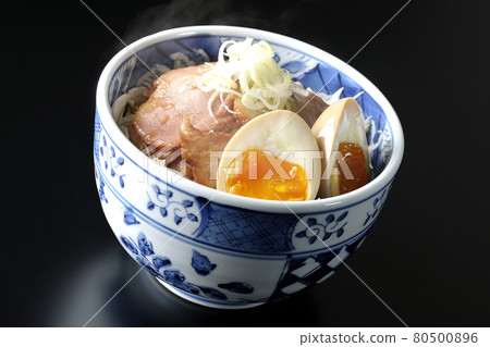 A steaming roast pork bowl topped with shredded cabbage, flavored balls and green onions, shot on a black background A steaming roast pork bowl topped with shredded cabbage, flavored balls and green onions, shot on a black background 80500896