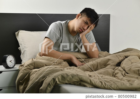 Depressed young Asian man sitting in bed cannot sleep from insomnia Depressed young Asian man sitting in bed cannot sleep from insomnia 80500982