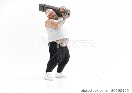 Happy fat man with big belly and tattos in sports wear with exercise mat 80502193