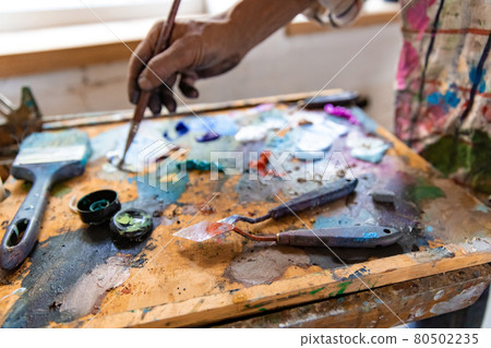Closeup of hand mixing paint on palette at workshop 80502235