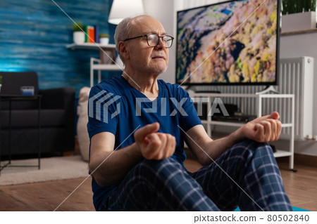 Healthy senior man sitting comfortable in lotus position on yoga mat with closed eyes 80502840