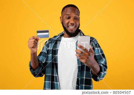Happy African Male Holding Credit Card And Phone, Yellow Background 80504507