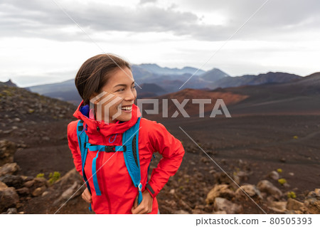 Hiking Asian woman in outdoor volcano landscape walking in Hawaii. Happy hiker on trek with backpack and red rain jacket. 80505393