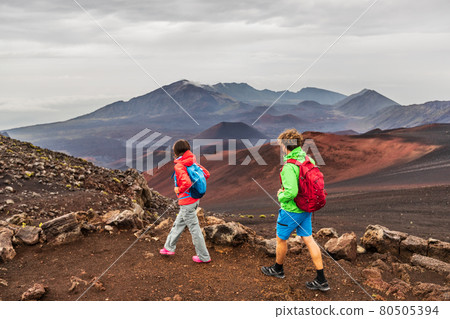 Hawaii volcano hikers people walking hiking on mountains in Haleakala volcanic background landscape. Two young tourists couple on trek hike outdoors. Hawaii volcano hikers people walking hiking on mountains in Haleakala volcanic background landscape. Two young tourists couple on trek hike outdoors. 80505394