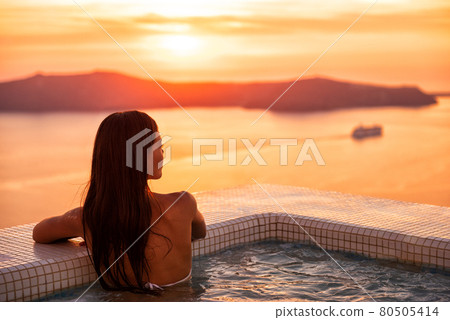 Luxury wellness spa resort pool woman relaxing in jacuzzi swimming at sunset in Europe Santorini hotel travel destination. Summer holiday. Luxury wellness spa resort pool woman relaxing in jacuzzi swimming at sunset in Europe Santorini hotel travel destination. Summer holiday. 80505414