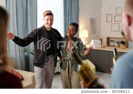 Joyful young intercultural couple meeting their friends with bottles of wine 80506011