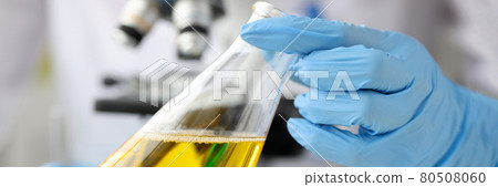 Scientist chemist holding glass flask with yellow liquid in front of microscope closeup Scientist chemist holding glass flask with yellow liquid in front of microscope closeup 80508060
