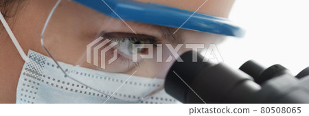 Woman chemist in goggles and mask looking through microscope closeup Woman chemist in goggles and mask looking through microscope closeup 80508065