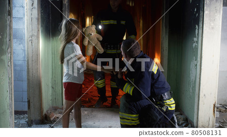Firemen speaking and giving toy to girl 80508131