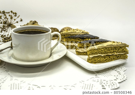 Seashells, dried flowers near a white cup with black coffee and a white dish with pieces of cream cakes lie on a white paper lace napkin. 80508346