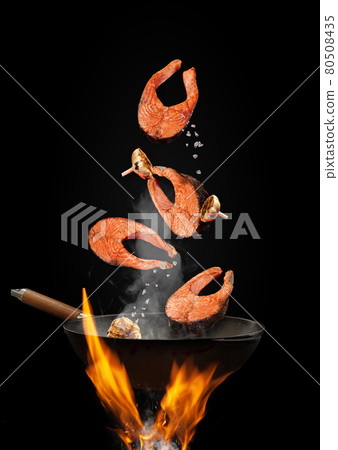 Wok pan with smoke above fire is frying salmon steaks with garlic against black studio background. Cooking concept. Close up 80508435