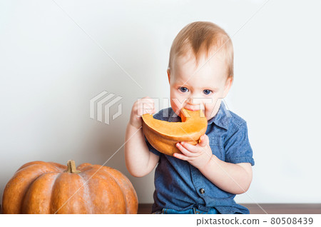 Baby in denim overalls and pumpkin. Toddler and concept of pumpkin puree, harvest, food allergies, healthy eating and first feeding. 80508439