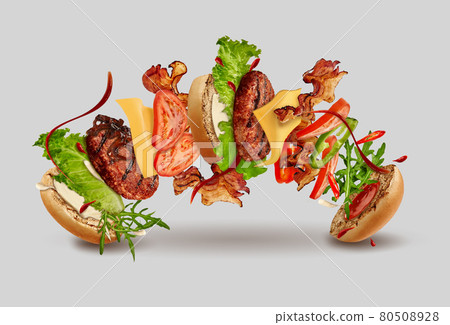 Burger with flying ingredients against gray background. Ham, beef cutlet, cheese, ketchup, mayonnaise, vegetables and greens. Close up, copy space 80508928