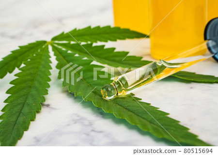 Cannabis oil in the vials with dropper tube and green leaf on marble table.  80515694