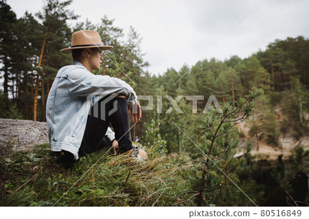 Stylish man sitting on edge of rocky slope among woods 80516849