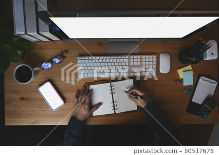 Overhead shot man making note on notebook and working with computer. Overhead shot man making note on notebook and working with computer. 80517678