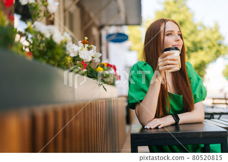 Portrait of attractive young woman enjoying tasty cup of coffee sitting at table in outdoor cafe terrace in summer day. Portrait of attractive young woman enjoying tasty cup of coffee sitting at table in outdoor cafe terrace in summer day. 80520815