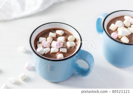 Hot chocolate with marshmallows in a blue enamel mug on white table. Hot chocolate with marshmallows in a blue enamel mug on white table. 80521121